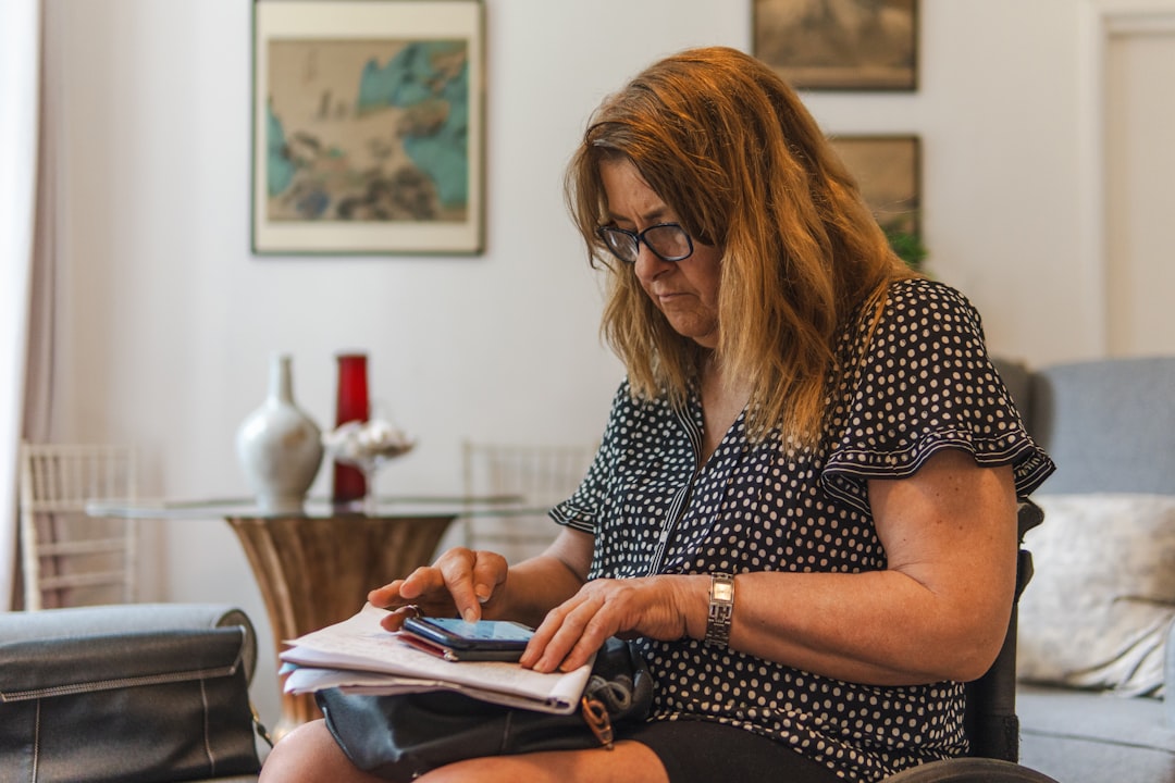 Older woman reviewing financial paperwork and writing notes at home.